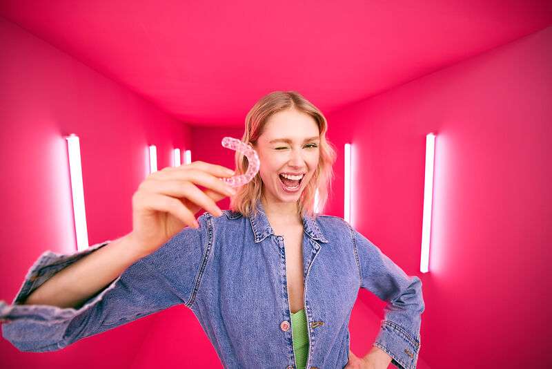 [CRO] Blond - Woman - Hand in Aligner - Winking at the camera - Pink - Light - Background - Desktop