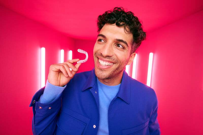 [CRO] Man - Brunette - Curly hair - Smile - Aligner - Looking right - Blue - Jacket - T-shirt - Pink - Light - Background - Desktop